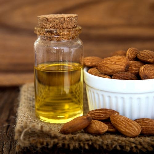 Mandelöl in einer Glasflasche mit Korken mit einer weißen Porzellanschale gefüllt mit Mandeln rechts daneben.